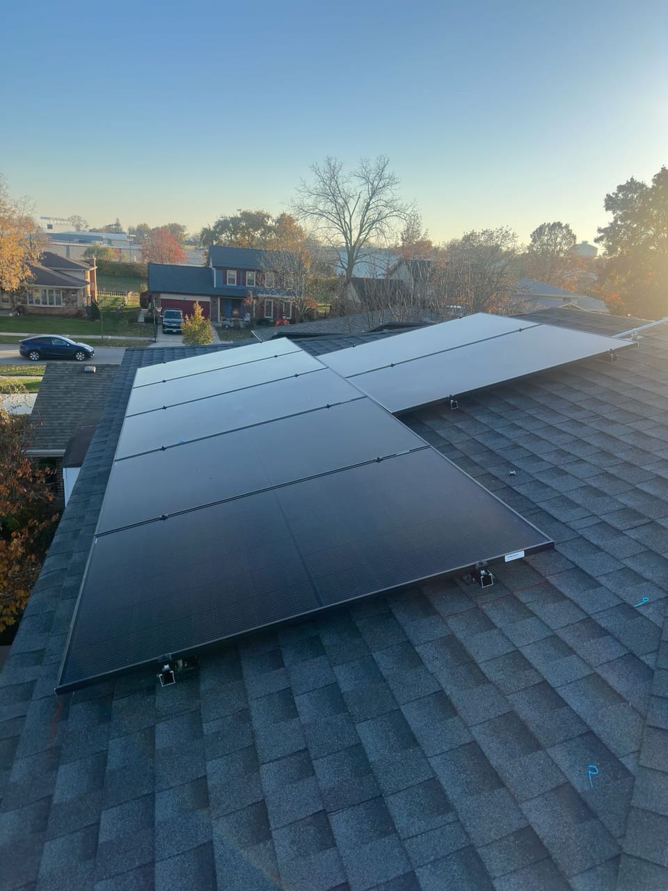 Solar panel array on a shingle roof at dusk with the neighborhood beyond