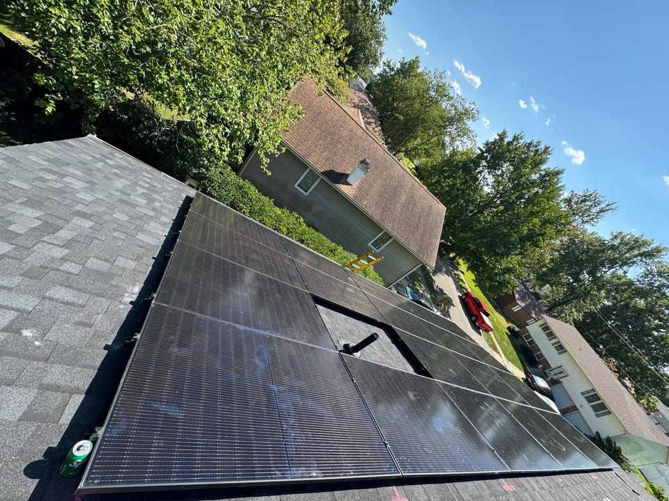 Solar array running along a shingle roofline, framed by trees
