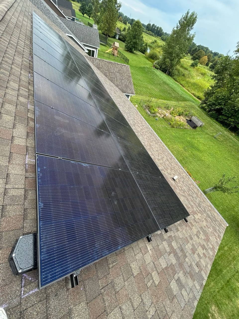 Solar panel array on a shingle roof overlooking a lawn and trees