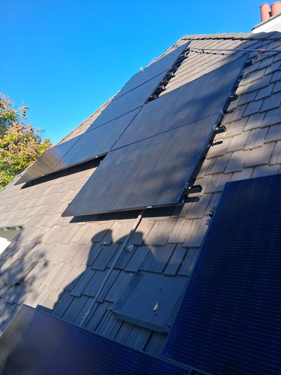 Solar panel array on a steep shingle roof against a blue sky