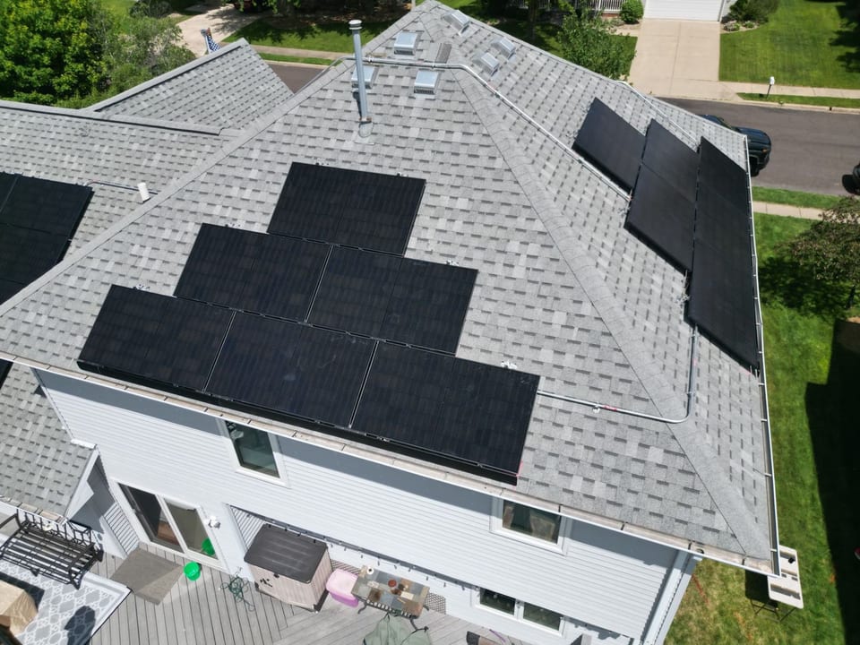 Aerial view of a white two-story home with black solar panels across two roof faces
