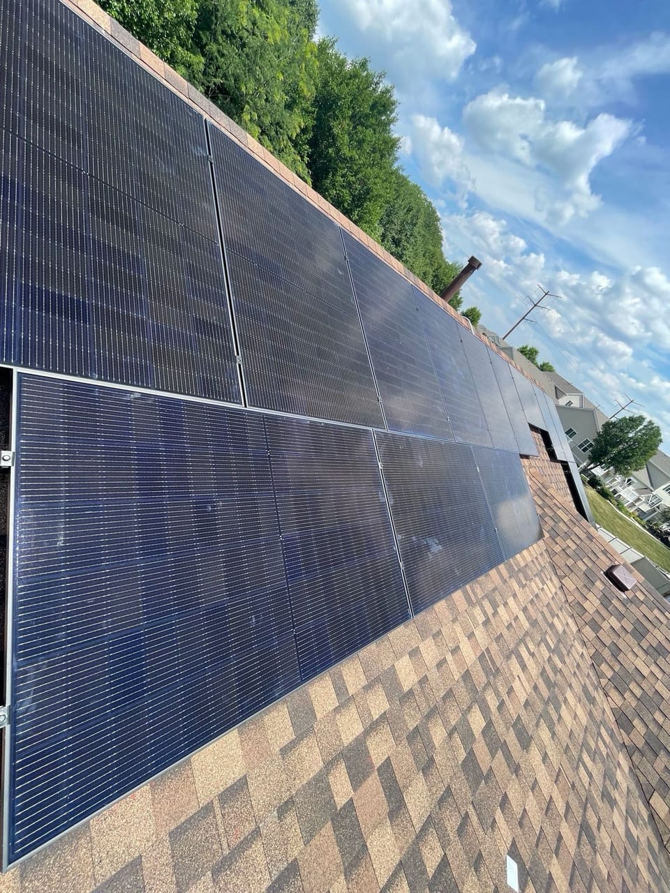 Solar panels running along a roof slope beside mature trees